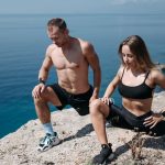 A man and a woman in sportswear stretching by the seaside on a sunny day.